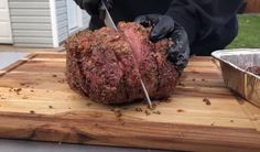 a person in black gloves cutting up a large steak on a wooden board with a knife