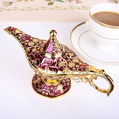 a gold and red teapot sitting on top of a table next to a cup of coffee