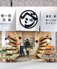 two people standing in front of a store with signs on the wall and produce section