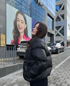 a woman standing on the sidewalk in front of a building with a large advertisement behind her