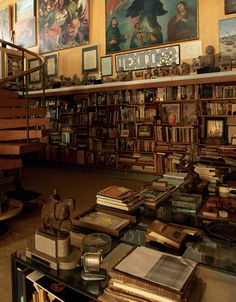 a room filled with lots of books next to a stair case full of pictures and paintings