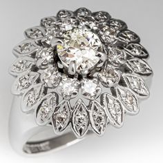 a fancy ring with an oval diamond center surrounded by smaller round brilliant cut diamonds in white gold