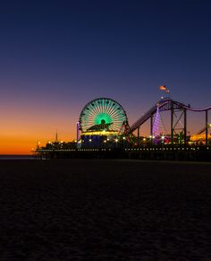 an amusement park at night with the ferris wheel lit up