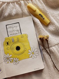 a yellow camera sitting on top of a notebook next to a pen and flower pot