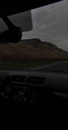 the dashboard of a car on a road with hills in the distance and dark clouds