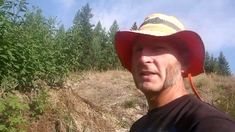 a man wearing a red hat standing in front of some bushes and trees on a sunny day