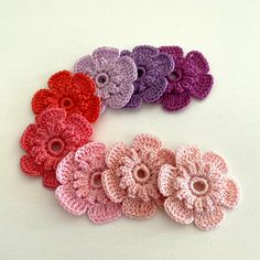 six crocheted flowers arranged in rows on a white surface with one flower facing the camera