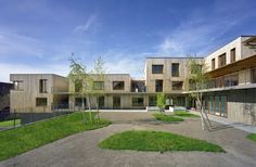 an empty courtyard with grass and trees in the foreground, surrounded by apartment buildings