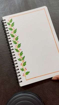 a hand holding a spiral notebook with holly designs on it