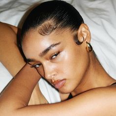 a woman laying on top of a bed next to a white sheet with her hands behind her head