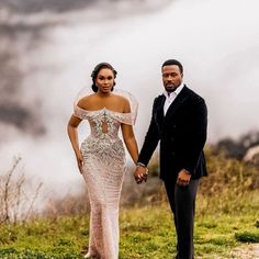 a man and woman holding hands while standing on top of a grass covered hill with clouds in the background