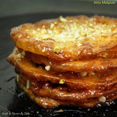 a stack of food sitting on top of a black plate covered in sauce and nuts