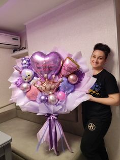 a woman standing next to a bouquet of balloons and teddy bears on a bench in a room