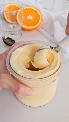 a person is holding a spoon in a jar with oranges and cream on the table