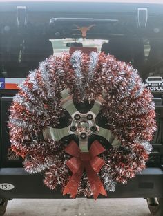 a christmas wreath on the back of a black truck with red bows and silver tinsel