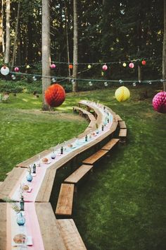 a long wooden bench sitting in the middle of a lush green field with paper lanterns hanging from it's sides