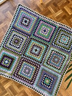 a crocheted blanket is sitting on the floor next to a potted plant