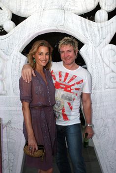 two people standing next to each other in front of a white wall with carvings on it