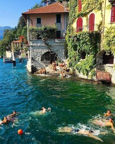 several people swimming in the water near some houses and buildings with ivy growing on them