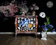 a vase with flowers on top of it next to a wooden cabinet and wallpaper