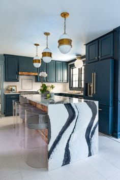 a kitchen with marble counter tops and dark green cabinets, along with two pendant lights