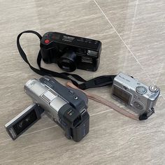 two cameras sitting on the ground next to each other, one has a strap around it's neck