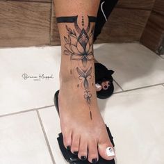 a woman's foot with a flower tattoo on her left leg and black sandals