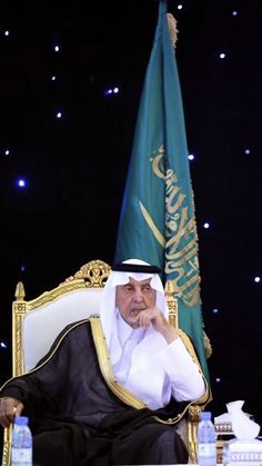 a man sitting on top of a white chair next to a green and blue flag