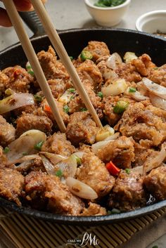 someone is holding chopsticks over some food in a pan with meat and vegetables