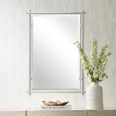 a white vase with some flowers and a mirror on a wall above the dresser in front of it