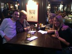 three people sitting at a table in a bar with drinks and papers on the table