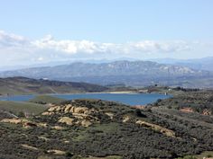 the mountains are covered in green grass and blue water, while there is a lake on the other side