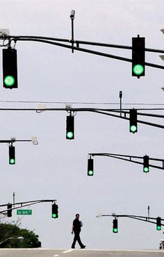 a man walking across a street next to green traffic lights with arabic writing on them