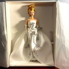 a barbie doll in a white dress inside a box on a wooden table with the lid open