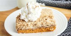 a piece of pie with whipped cream on top sits on a plate next to a glass of milk