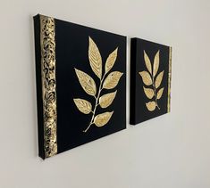 two black and gold paintings hanging on the wall next to each other with leaves painted on them