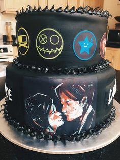 two tiered cake decorated with black frosting and pictures of people on it's sides