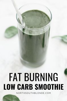 a glass filled with green smoothie sitting on top of a white table next to leaves