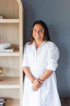 a woman standing next to a bookshelf with her arms crossed and smiling at the camera