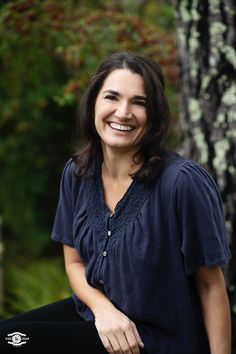 a woman sitting in front of a tree smiling