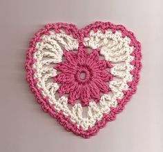 a crocheted heart hanging on the wall with pink and white trimmings