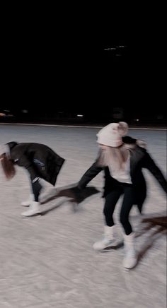 two people are skating on an ice rink at night with one person holding the other's hand