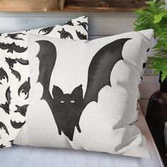 two pillows with bats on them are sitting on a bed next to a potted plant