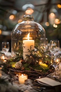 a table topped with a glass dome covered in greenery and lit candles