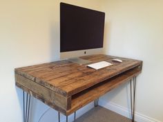 a desk with a computer on top of it in front of a wall mounted monitor