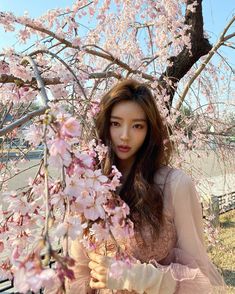 a woman standing under a tree with pink flowers