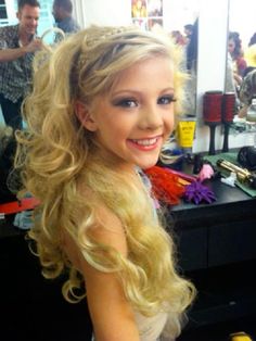 a woman with long blonde hair sitting in front of a mirror smiling at the camera