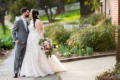 a bride and groom kissing in front of a building with flowers on the side walk