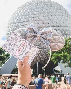 a hand holding up a disney mouse ears with the top of it's head in front of a building