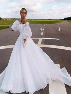 a woman in a white wedding dress standing on an airport runway with her arms behind her back